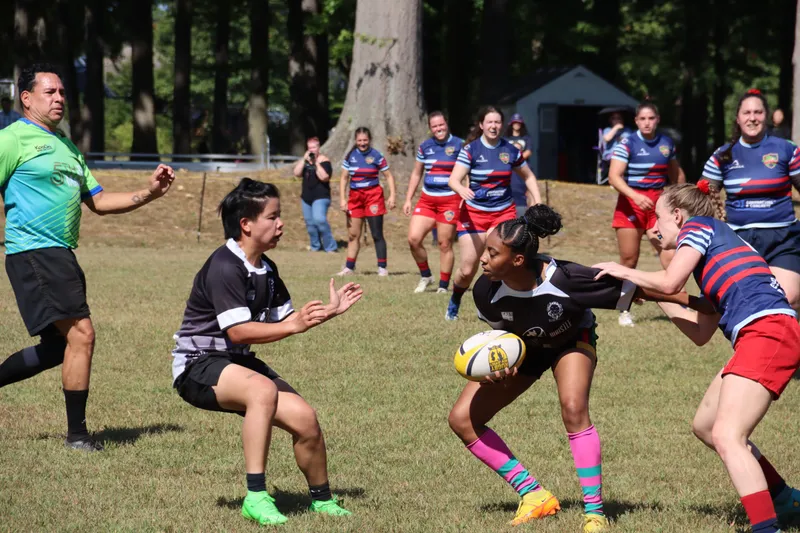 A Women's+ Lions player receives a pass under pressure from a defender in red