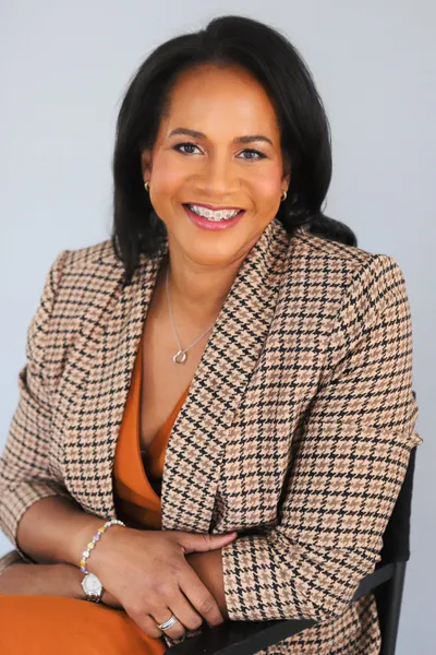 Koma Gandy, seated and smiling, in a houndstooth blazer