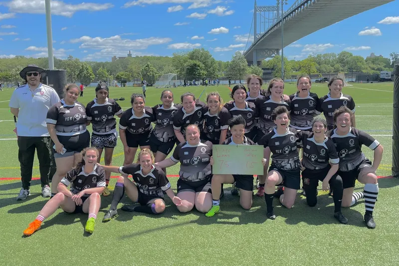 The Women's+ 15s squad gathered on the pitch after a match, a bridge behind them