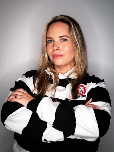 Jacquie Sinclair, arms folded, in a black and white hooped Village Lions jersey