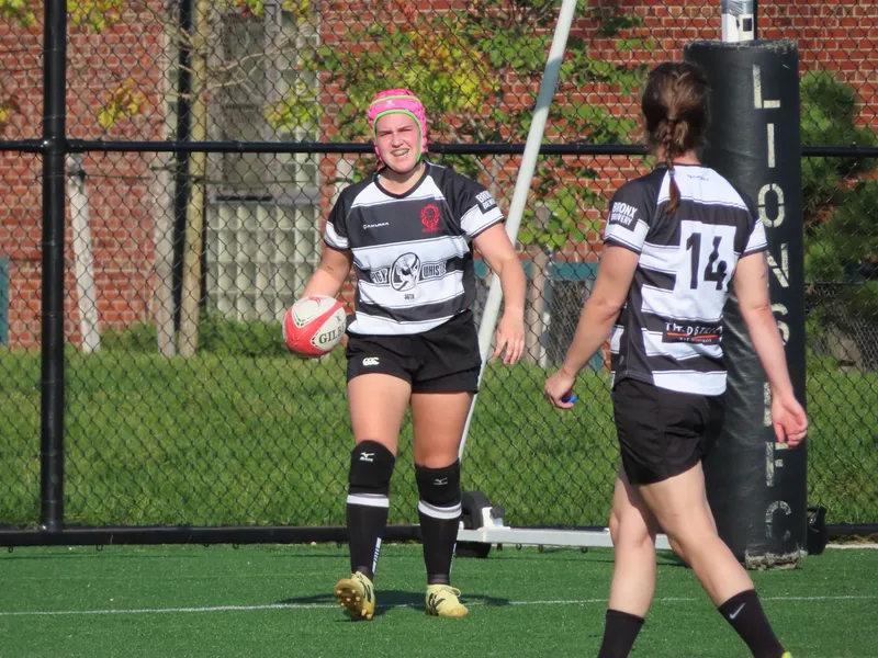 Two Women's+ Lions players walk back into position, one in a pink scrum cap with the ball