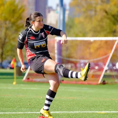 Stephanie Ruys de Perez taking a place kick in the Lions' black and red kit, on a pitch with the city skyline behind